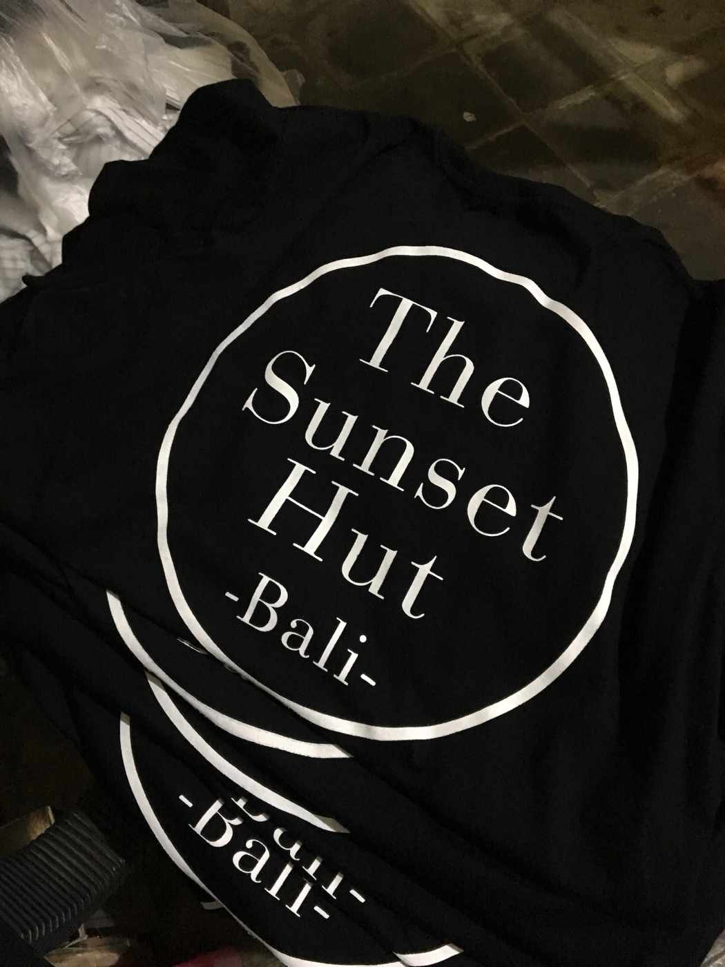 A stack of black café t-shirts with a large white circular logo print.