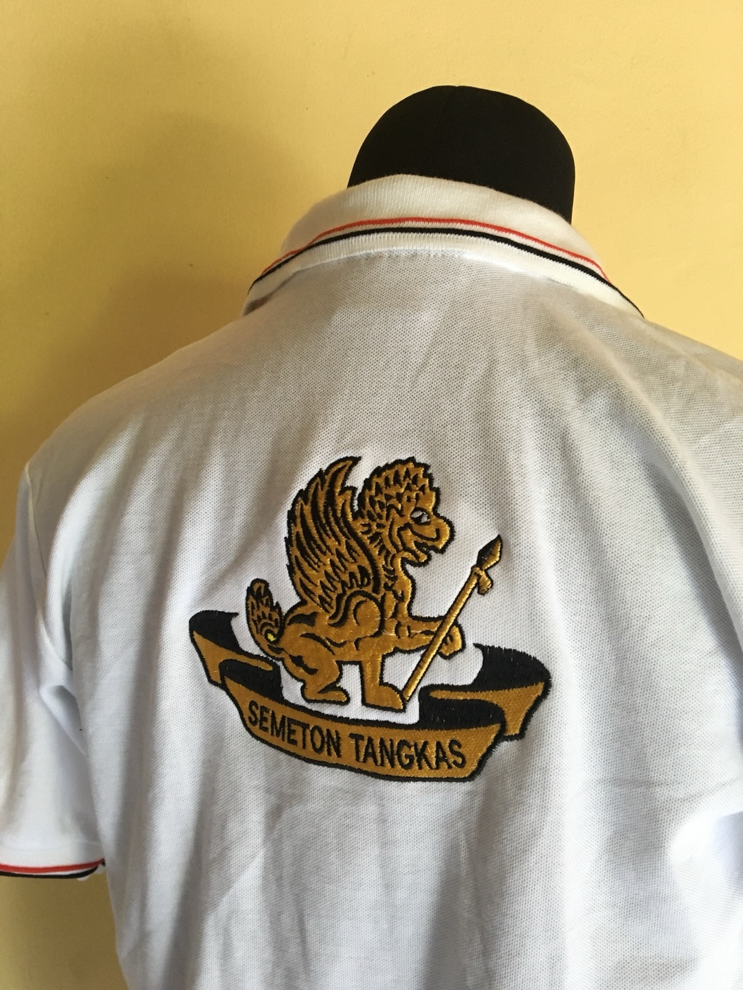 Back of a white polo on a mannequin with a gold embroidered crest.