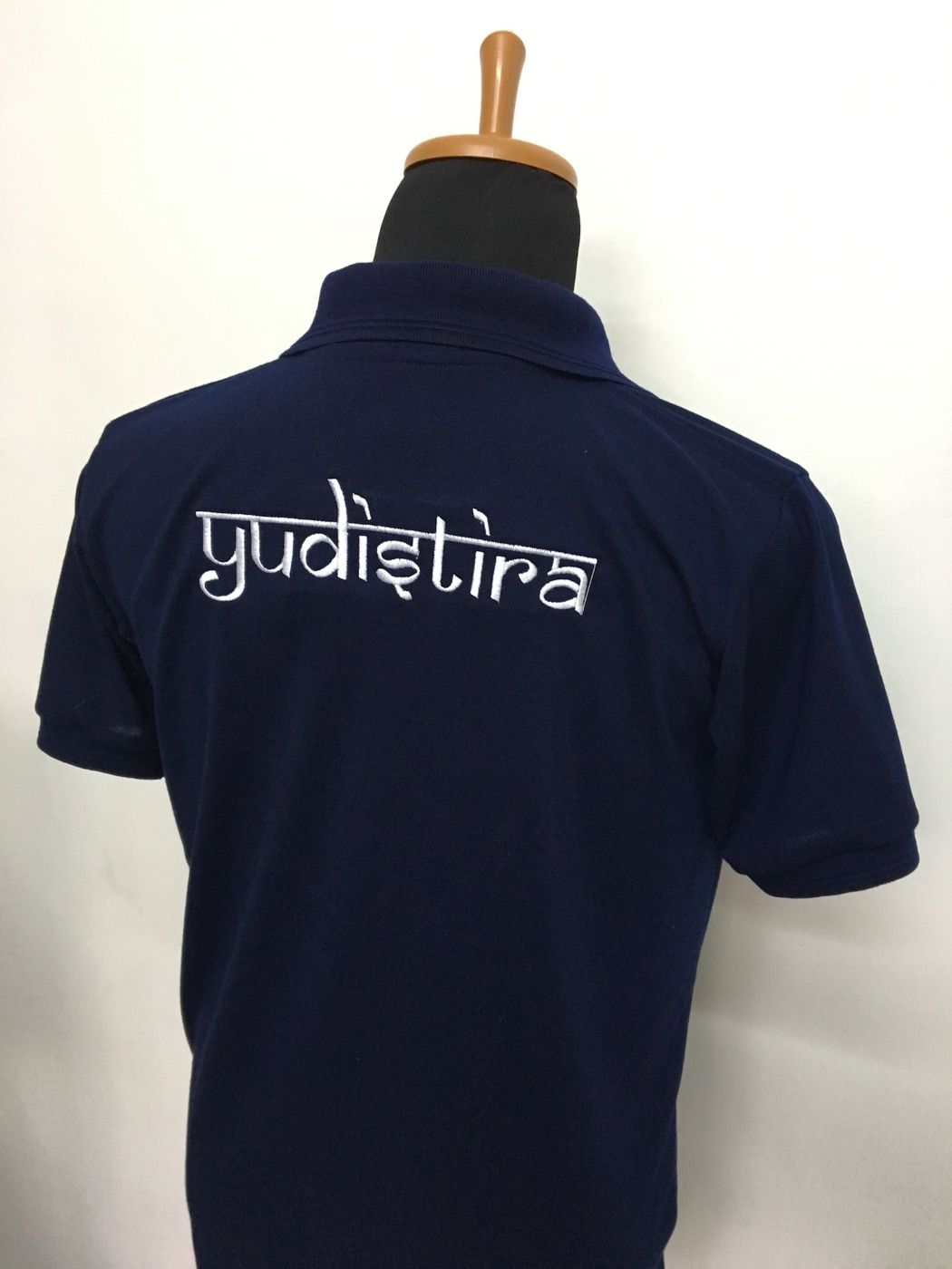 Back of a navy polo on a mannequin with white printed lettering.